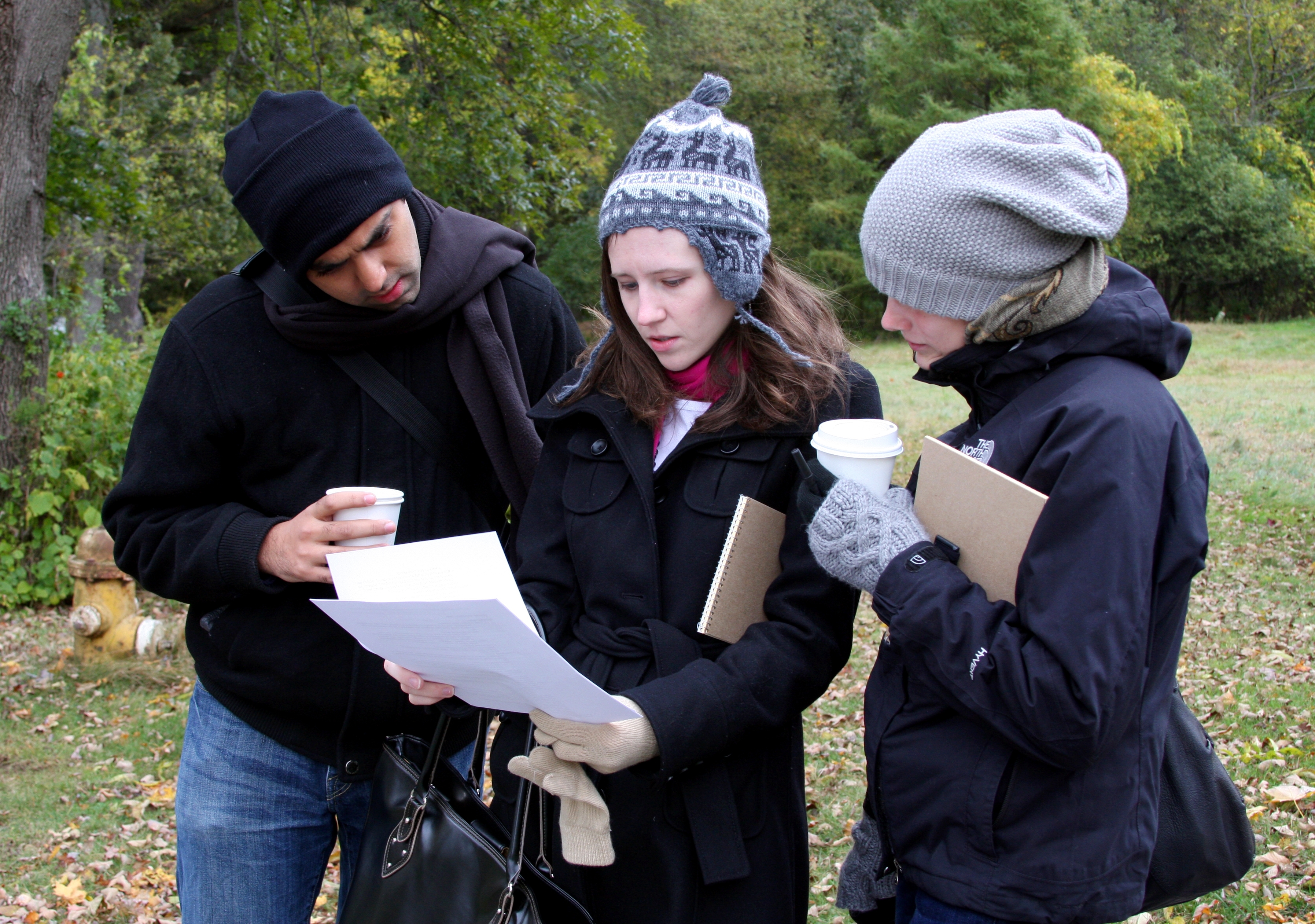 Three students outside look a piece of paper as they participate in a role play.