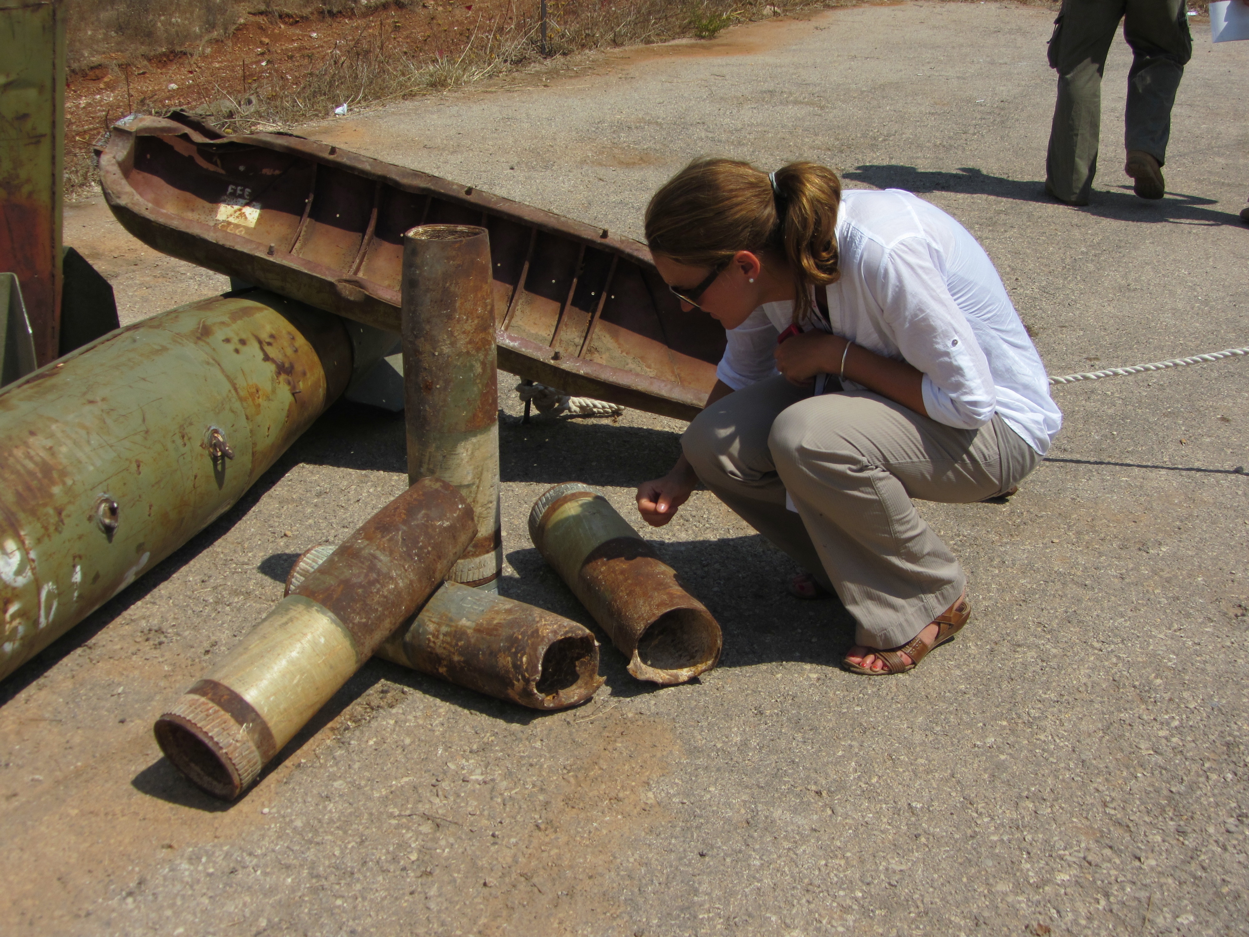 A woman crouches to examine rusty metal pieces that look like weapons.