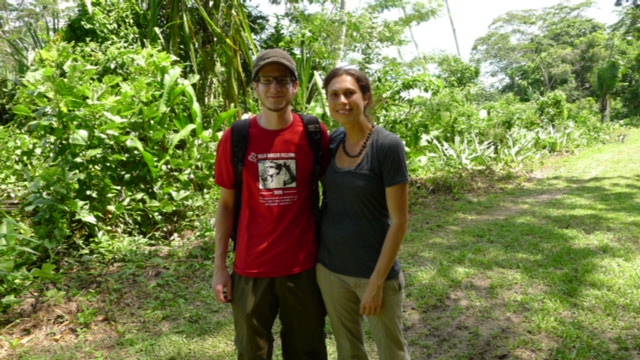 A young man and woman stand in front of lush forests.