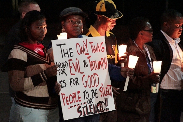 Five protestors in South Africa hold a sign that says, "The only thing needed for evil to triumph is for good people to be silent or silenced!!" The protest appears to be a candlelight vigil.