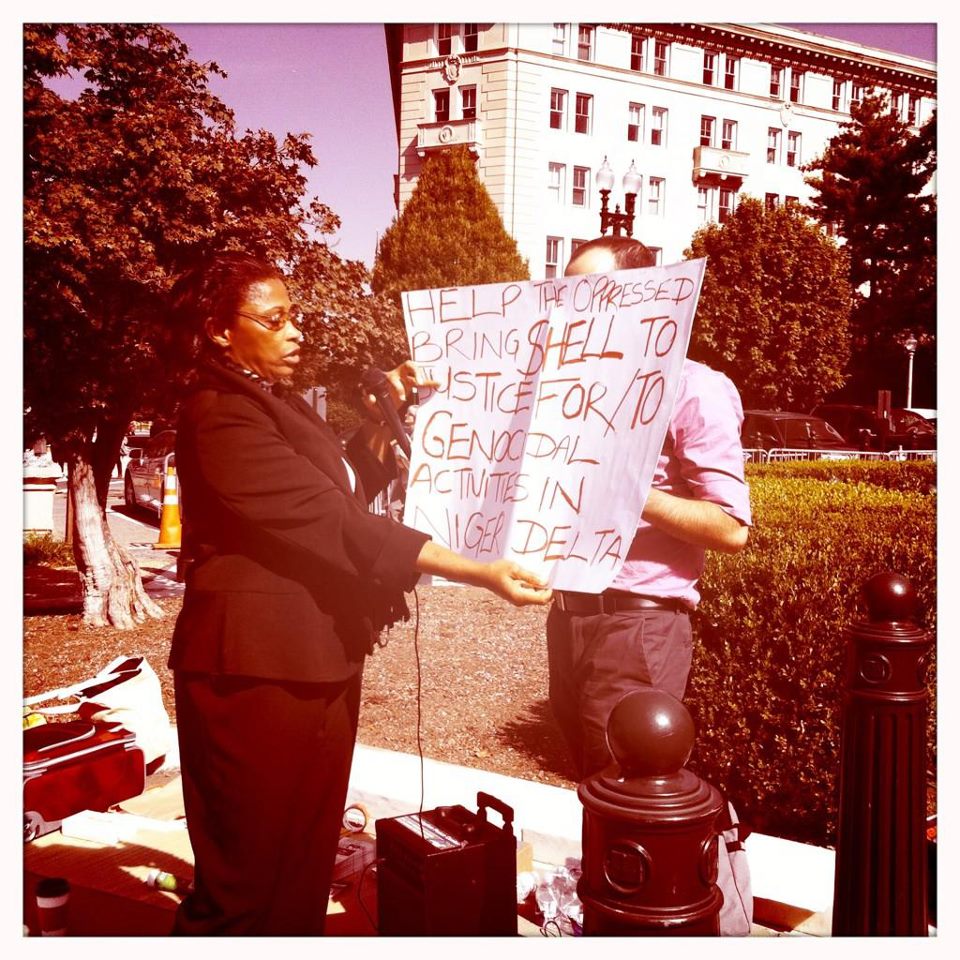 Esther Kiobel wears a pants suit, holding a sign outside the Supreme Court that says, "Help the oppressed bring shell to justice for genocidal activities in Niger Delta."