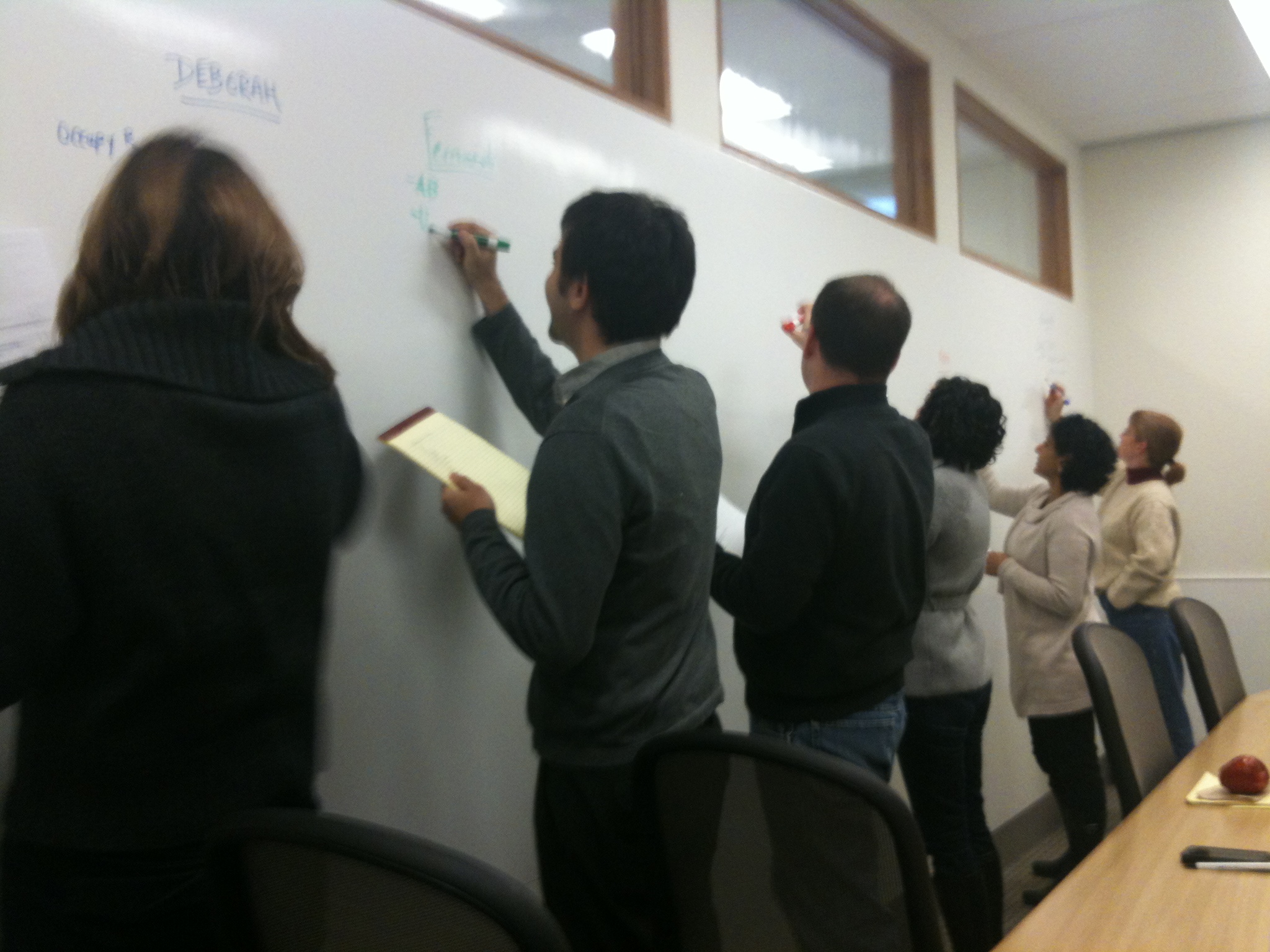 Six individuals write on a whiteboard.