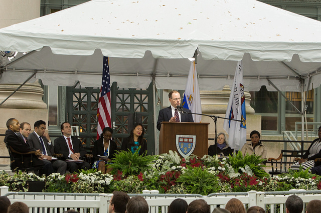 Tyler Giannini speaks at a podium under a white tent at Harvard Law School graduation.
