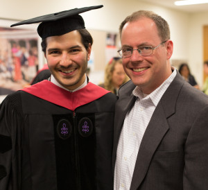 A man in a Harvard graduation robe smiles with a man in a suit.