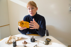 A woman sits in front of a table gesturing at various objects.
