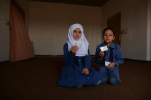 Two Syrian schoolmates hold up their MoI cards. Credit: Norwegian Refugee Council/Lian Saifi