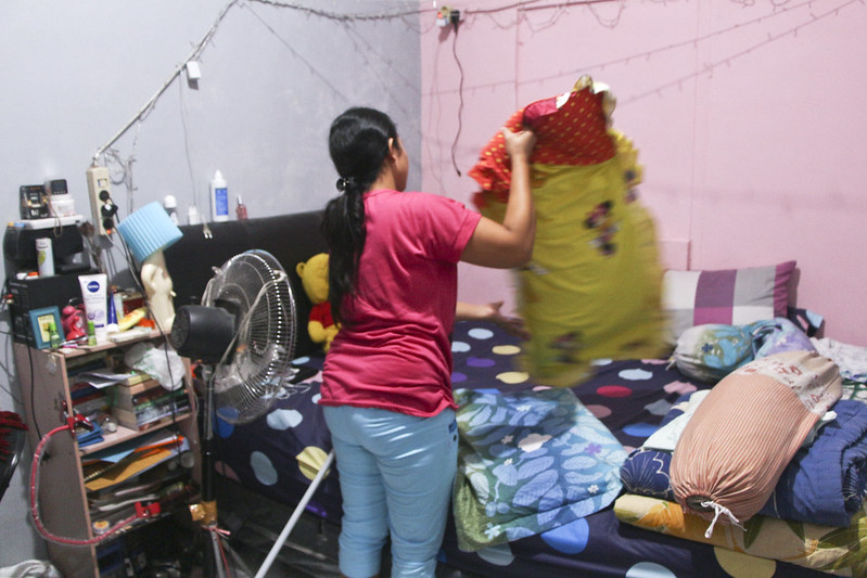 A woman makes a bed and prepares laundry in Indonesia.
