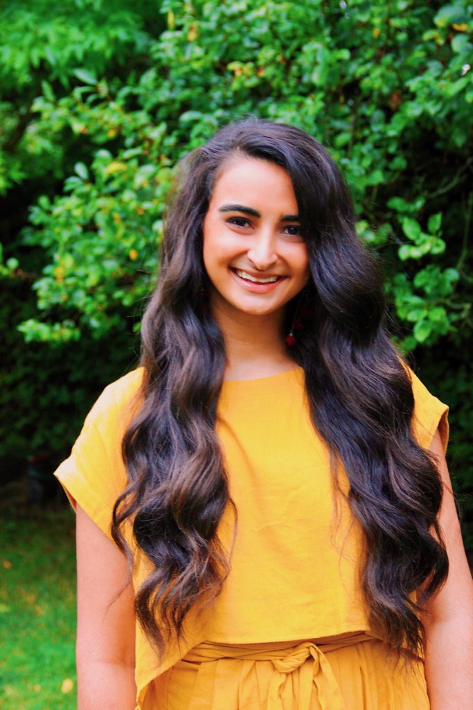 A woman wearing a yellow romper smiles.