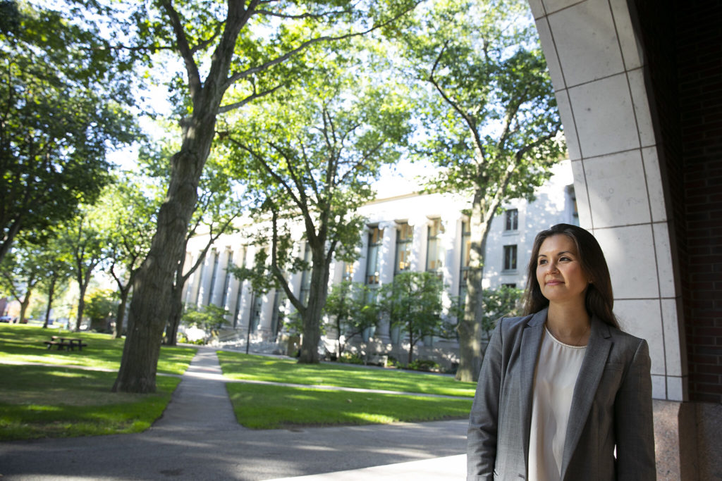 A woman wearing a gray blazer looks out into the distance under an arch in front of the Harvard Law library.