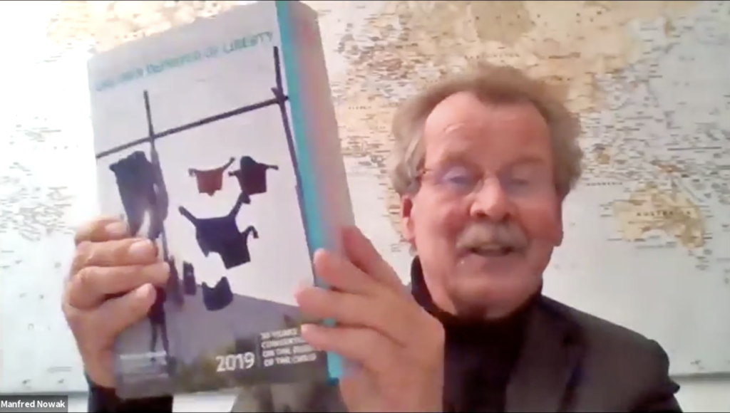A man holds a book up on zoom. There is a map behind him.
