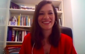 A woman with a red top smiles in front of a bookshelf behind her.