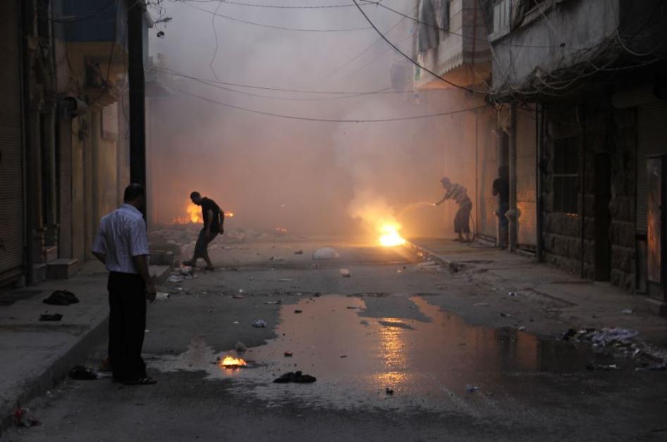 Men stand in an empty street that has been hit by incendiary weapons causing fires.