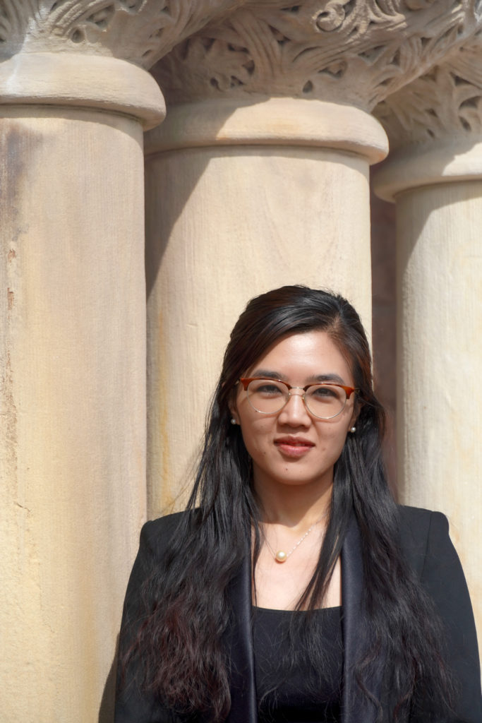 Rosalinn Zahau standing in front of pillars and wearing a black top and black blazer.