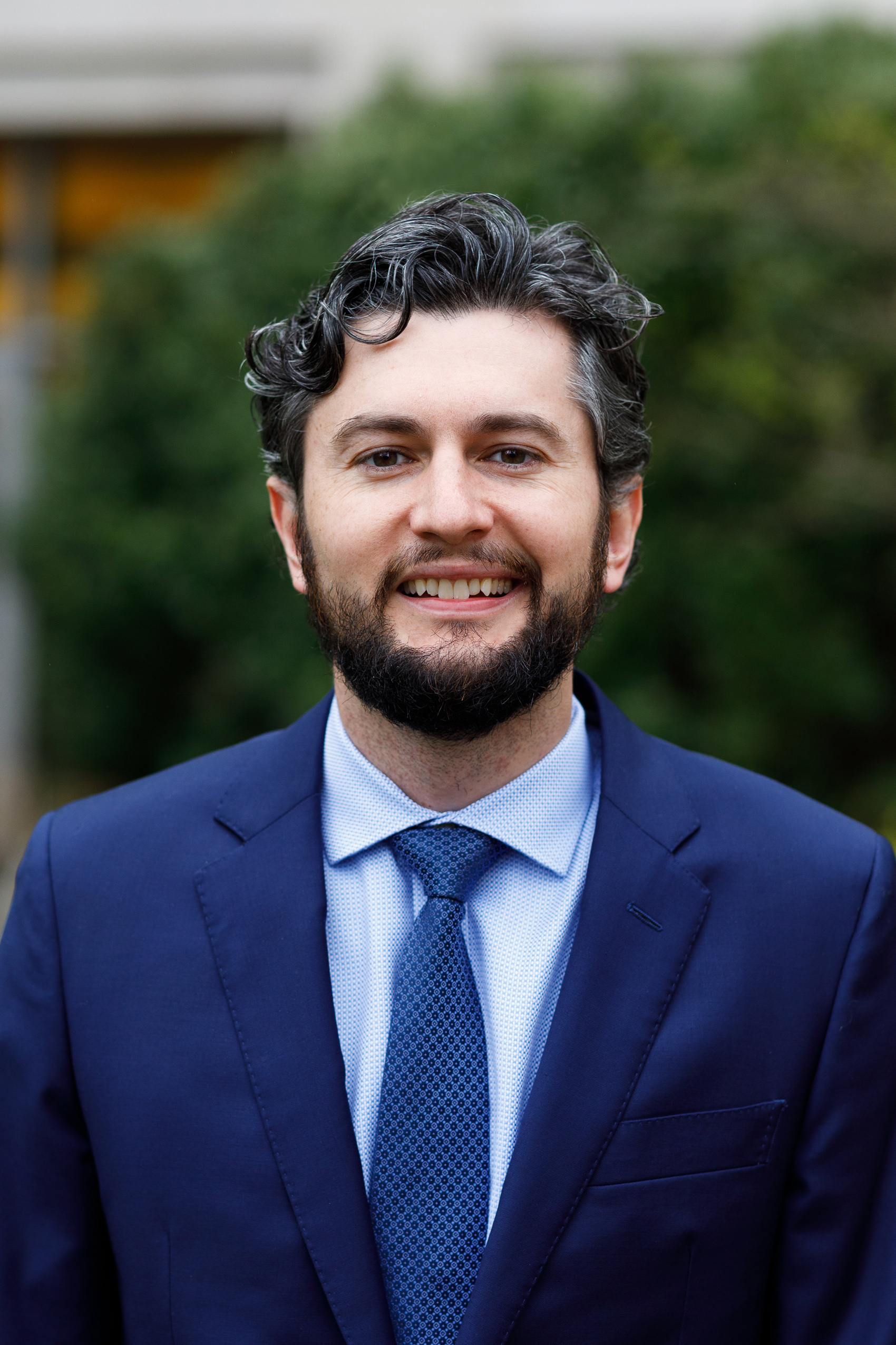 Andrew Santana wearing navy suit and tie smiling into camera.