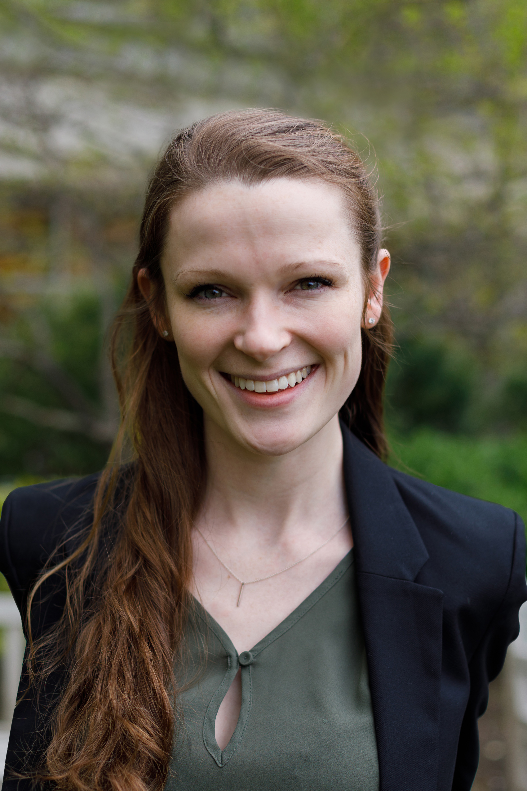 Madeleine Rogers wearing black jacket and olive-green shirt smiling into camera.  