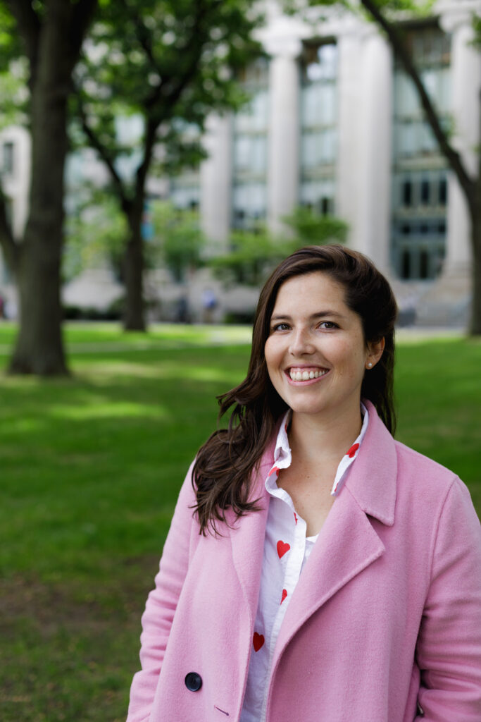 Maria Cecilia Ercole wearing a pink coat and smiling into the camera while standing in front of Harvard Law Langdell Library.