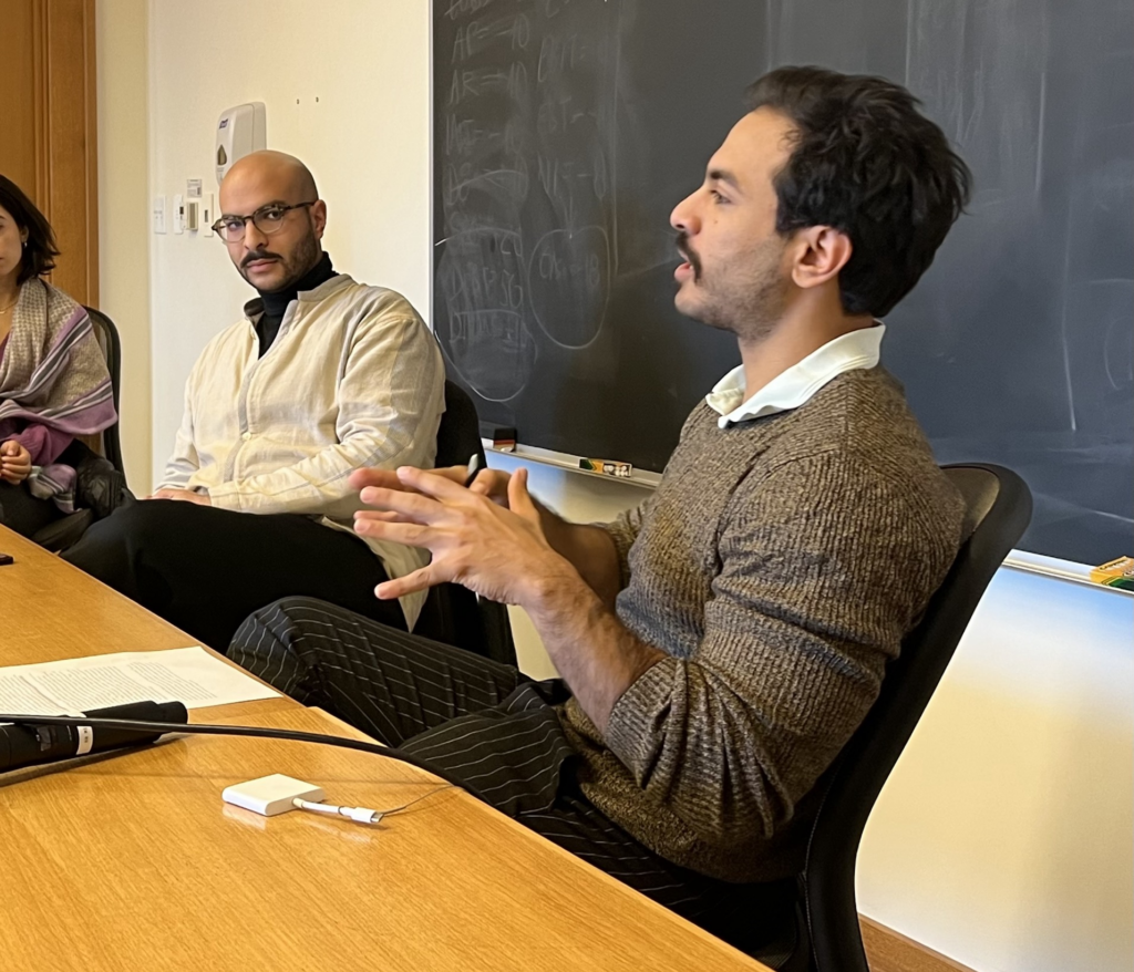 Speaker Nader Andrawos in conversation with moderator Omar Abdel-Ghaffar. They are both sitting at a table in front of a blackboard. 