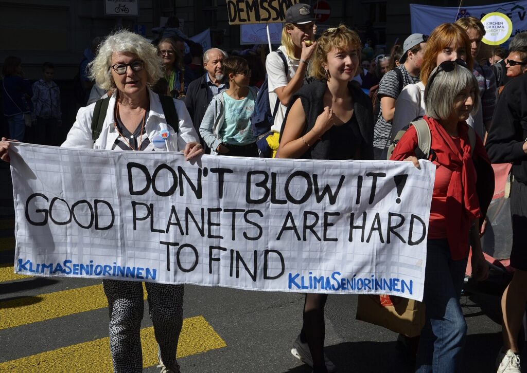 An elderly woman holding up a banner at a climate demonstration in Bern: "Don't blow it! Good planets are hard to find. KlimaSeniorinnen". Photo credit: Hadi. 