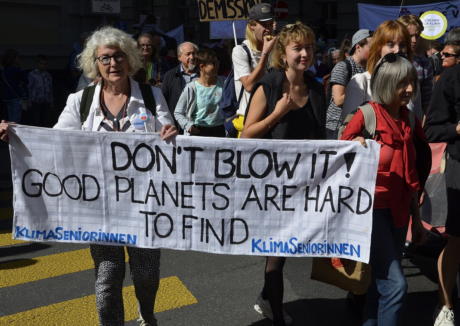 An elderly woman holding up a banner at a climate demonstration in Bern: "Don't blow it! Good planets are hard to find. KlimaSeniorinnen"