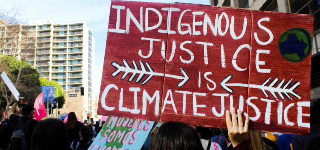 A person at a demonstration holding a sign saying "Indigenous justice is climate justice."