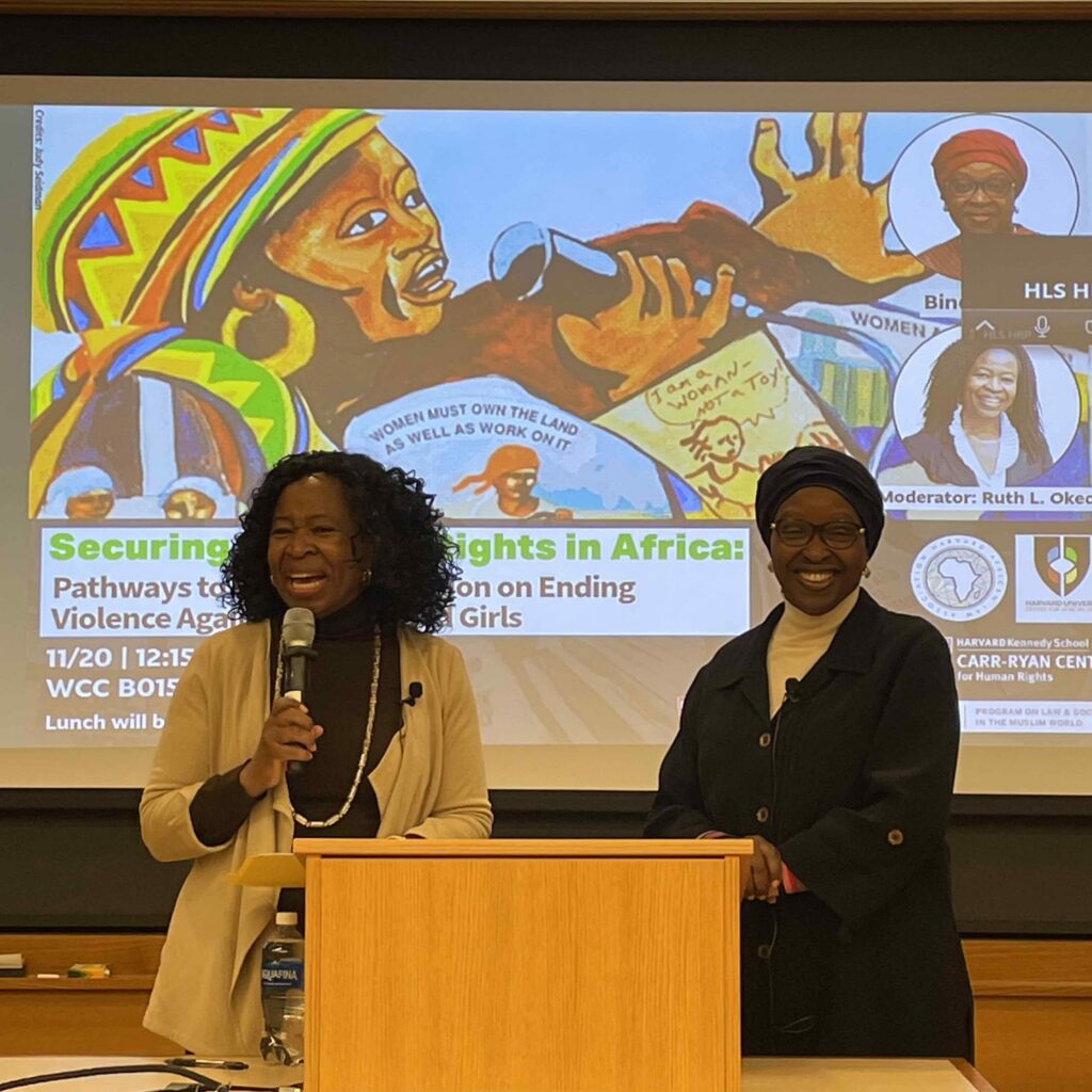 Two women standing by a podium in front of a projected presentation.