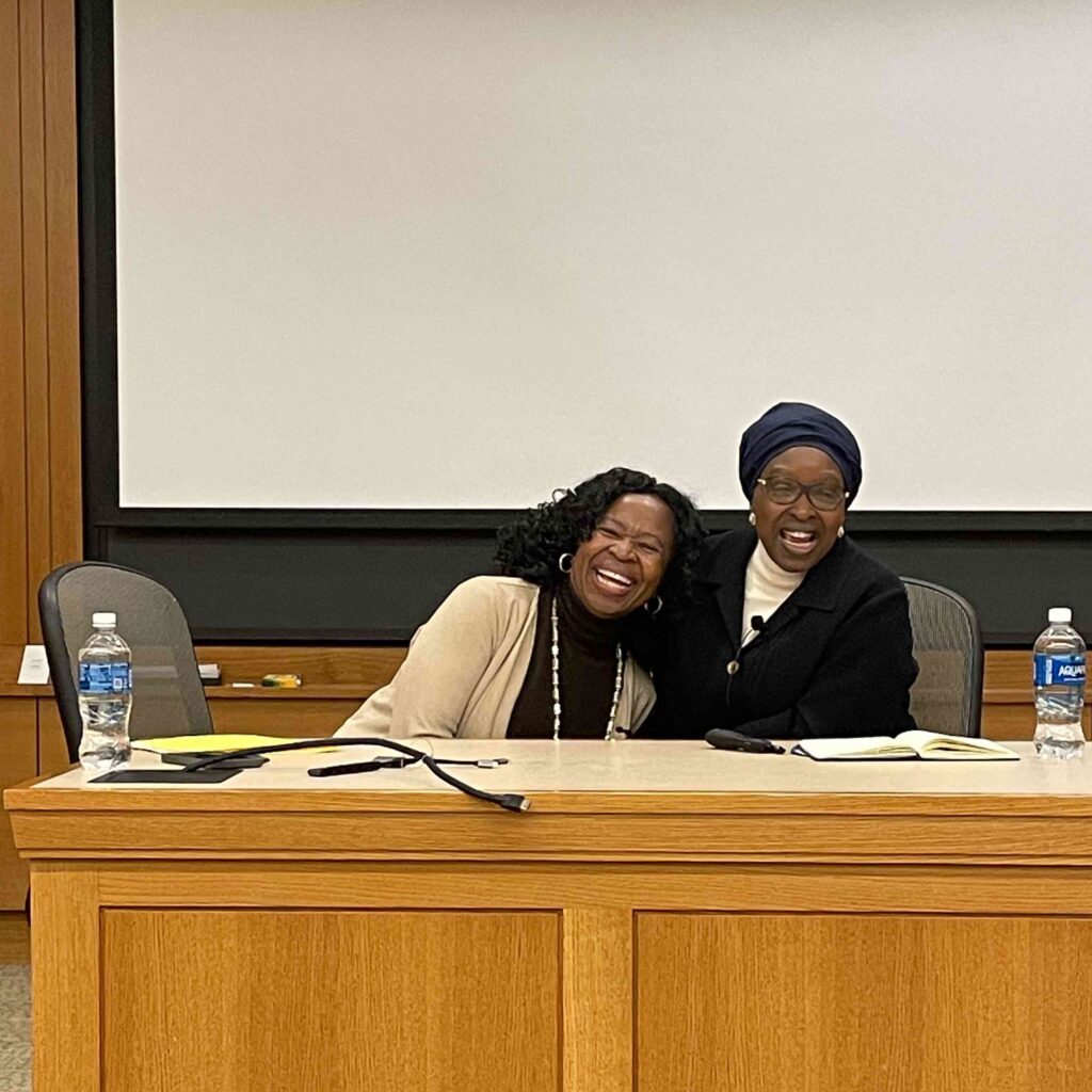 Two women smiling while embracing and sitting next to each other.