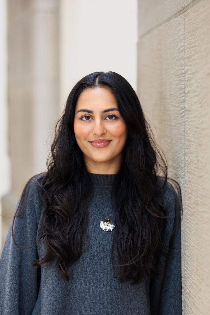Headshot of a woman wearing a grey sweater standing by a wall.
